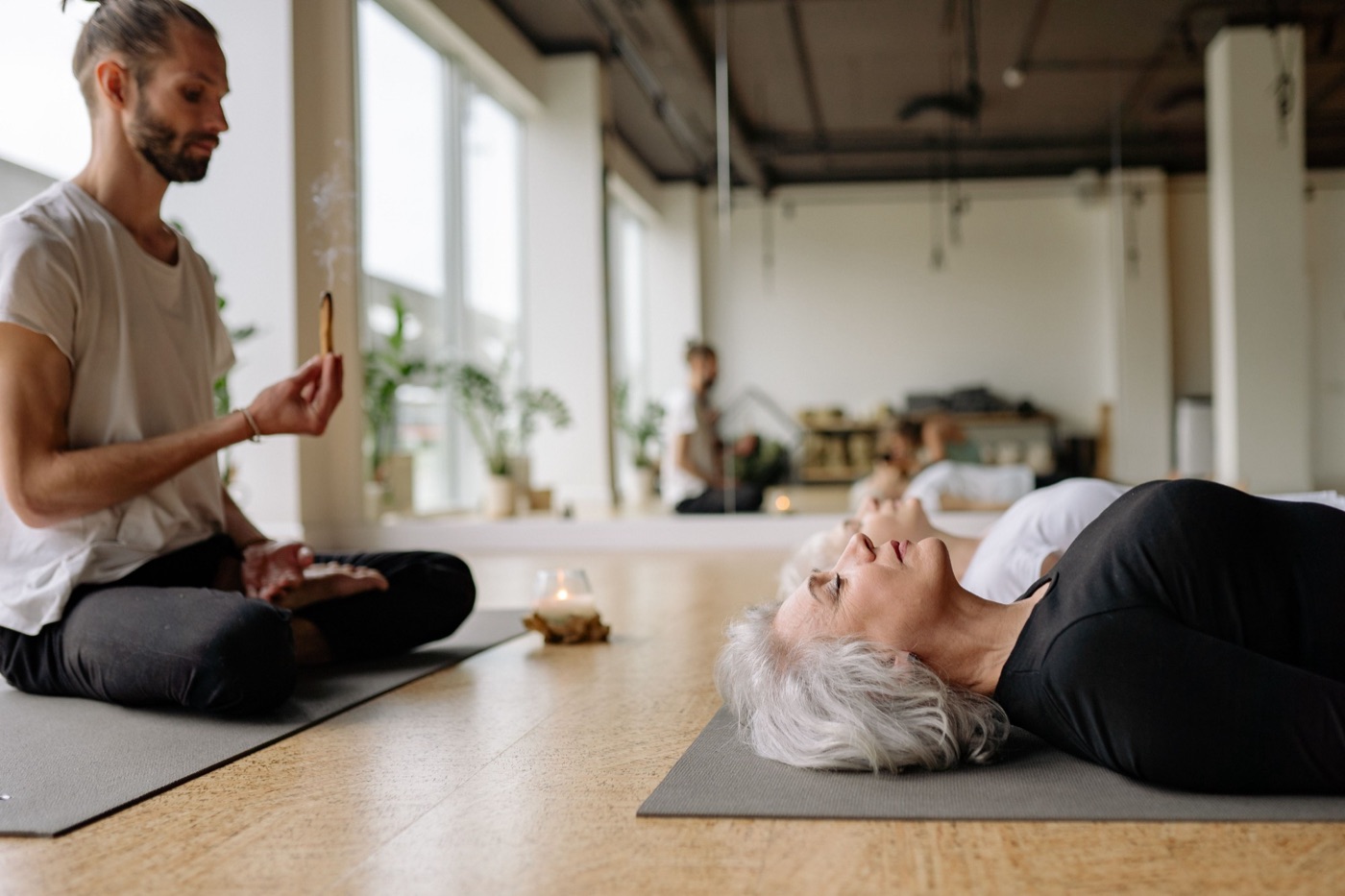 Eine Frau liegt entspannt mit geschlossenen Augen auf einer Yogamatte, daneben brennt eine Kerze